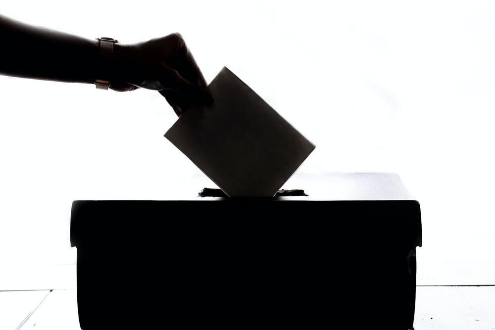 Sombra de una mano echando un voto en una urna electoral